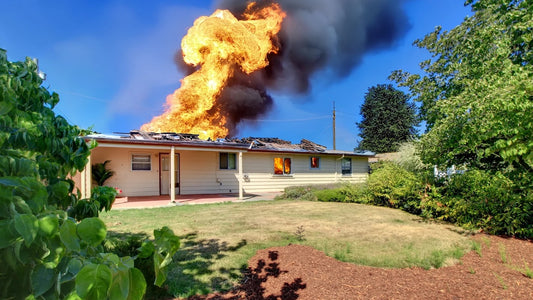 House on fire with flames and smoke against a clear blue sky.