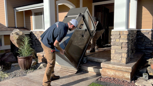 Two men moving a large safe into a house entrance.